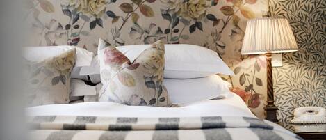 A bed with floral-patterned pillows, a striped blanket, and a bedside table with a lamp and a rotary phone.