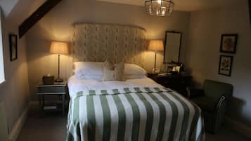 A neatly made bed with a striped bedspread, two bedside lamps, a nightstand with a lamp, a chair, and a hanging light fixture.