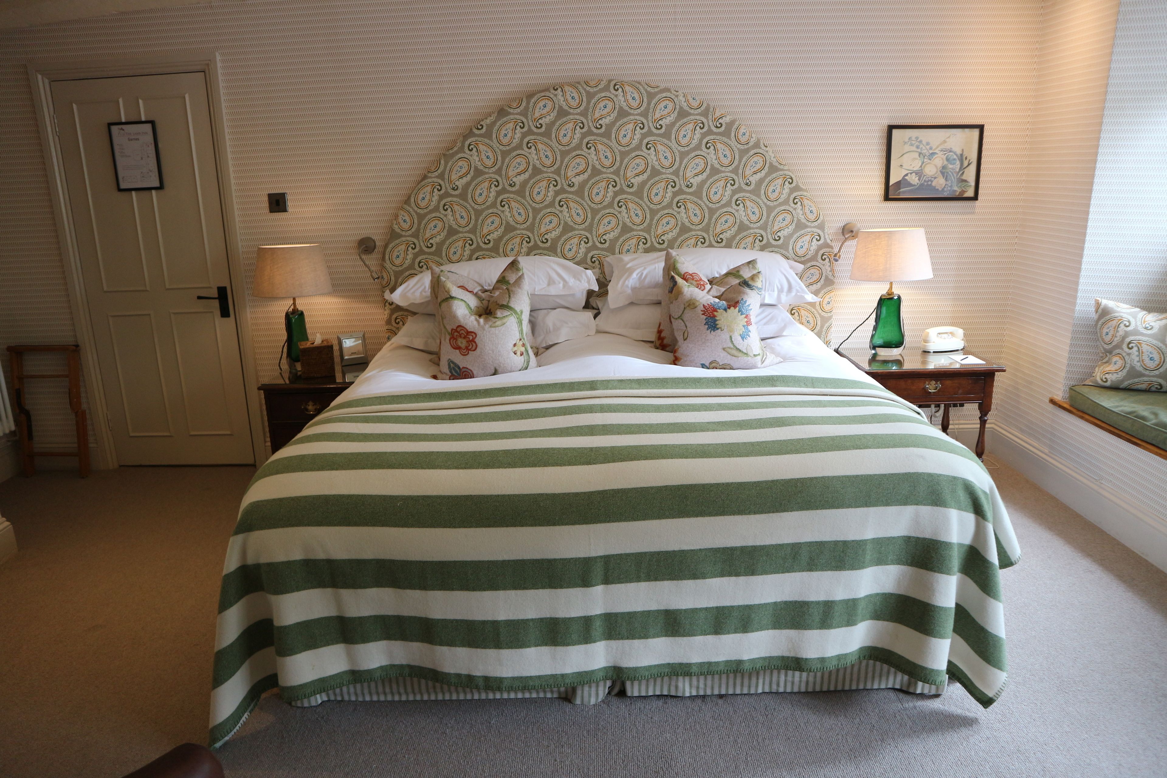 A neatly made bed with a striped bedspread, a patterned headboard, and two bedside lamps.