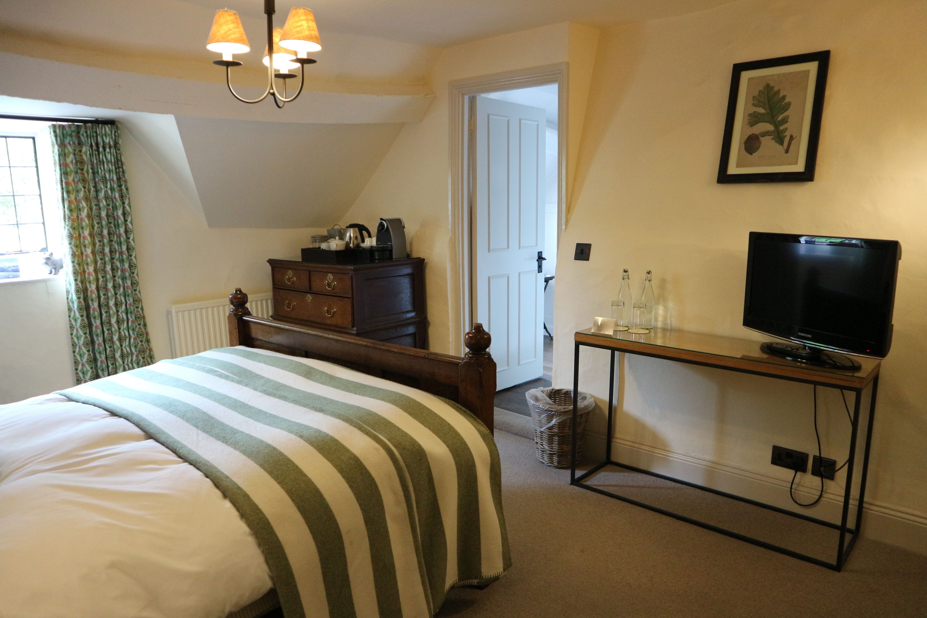 Een slaapkamer met een bed, een kaptafel, een televisie op een standaard en een deur naar een andere kamer.