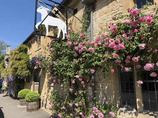 A building with a stone facade, pink roses, and a white horse sign. - The Lamb Inn (Burford)