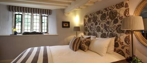 A bedroom with a large bed, a window with curtains, a bedside lamp, and a mirror on the wall.