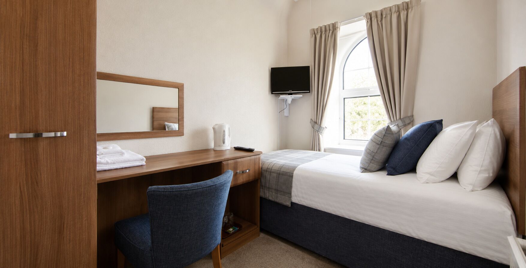A hotel room with a bed, a desk, a chair, a television, and a window with curtains.