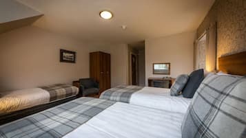 A room with three beds, a wooden wardrobe, a chair, and a small table with a lamp.