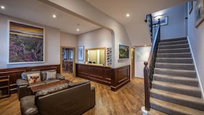 A spacious living room with a large sofa, a wooden coffee table, and a fireplace. There is a staircase with a wooden railing leading to an upper level.