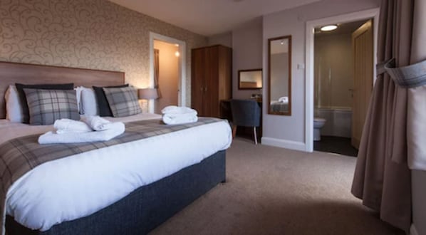 A hotel room with a large bed, a desk, a wardrobe, and a bathroom visible through an open door.