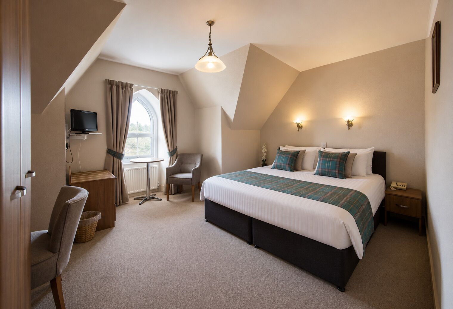 A bedroom with a bed, bedside tables, a desk, a chair, a television, and a window with curtains.