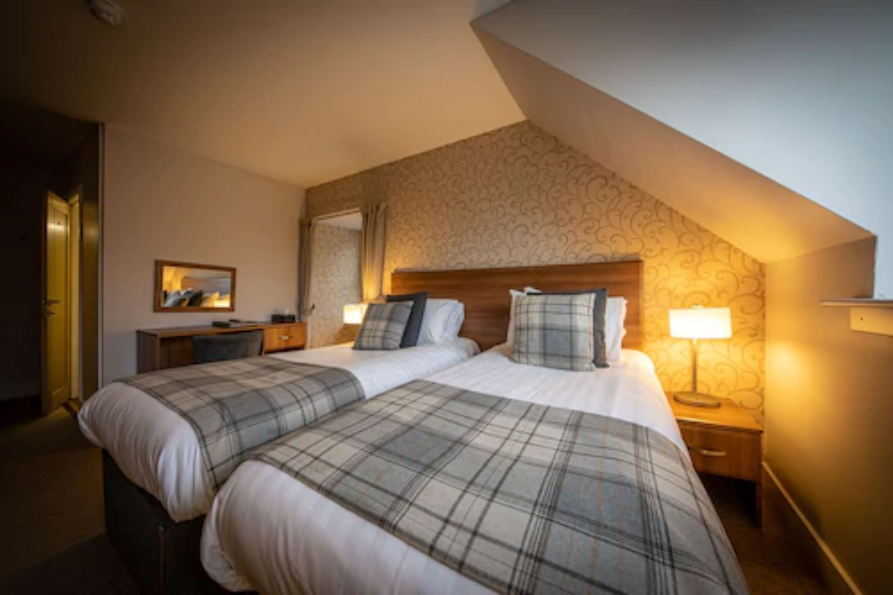 A hotel room with two beds, a desk, a chair, a lamp, and a mirror.
