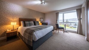 A hotel room with a large bed, a desk, a chair, and a window with a view.
