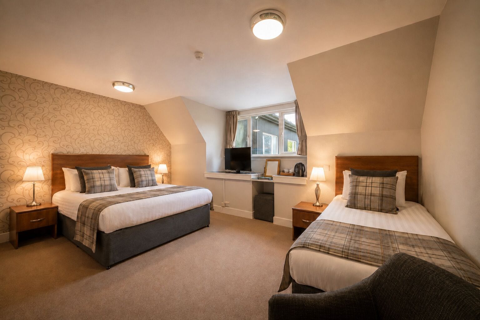 A hotel room with two beds, a desk, and a window.