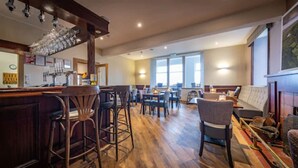 A spacious restaurant with wooden flooring, bar stools, and a mix of seating options including tables and chairs.