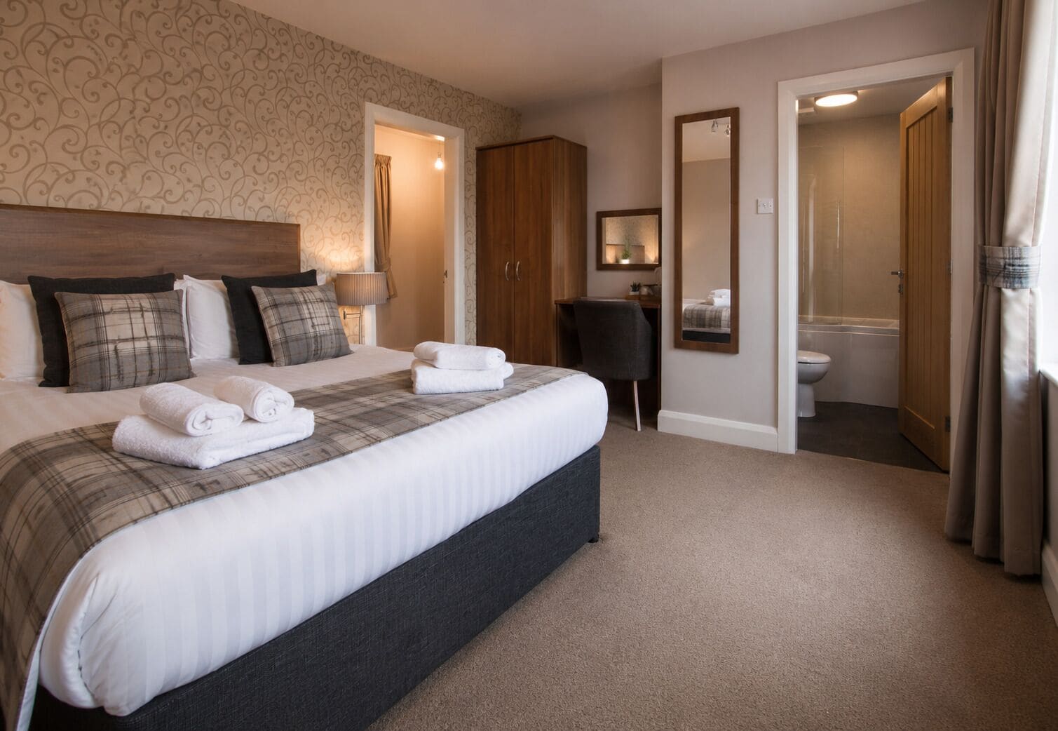 Habitación de hotel con una cama grande, un escritorio, una silla, un espejo y un baño.