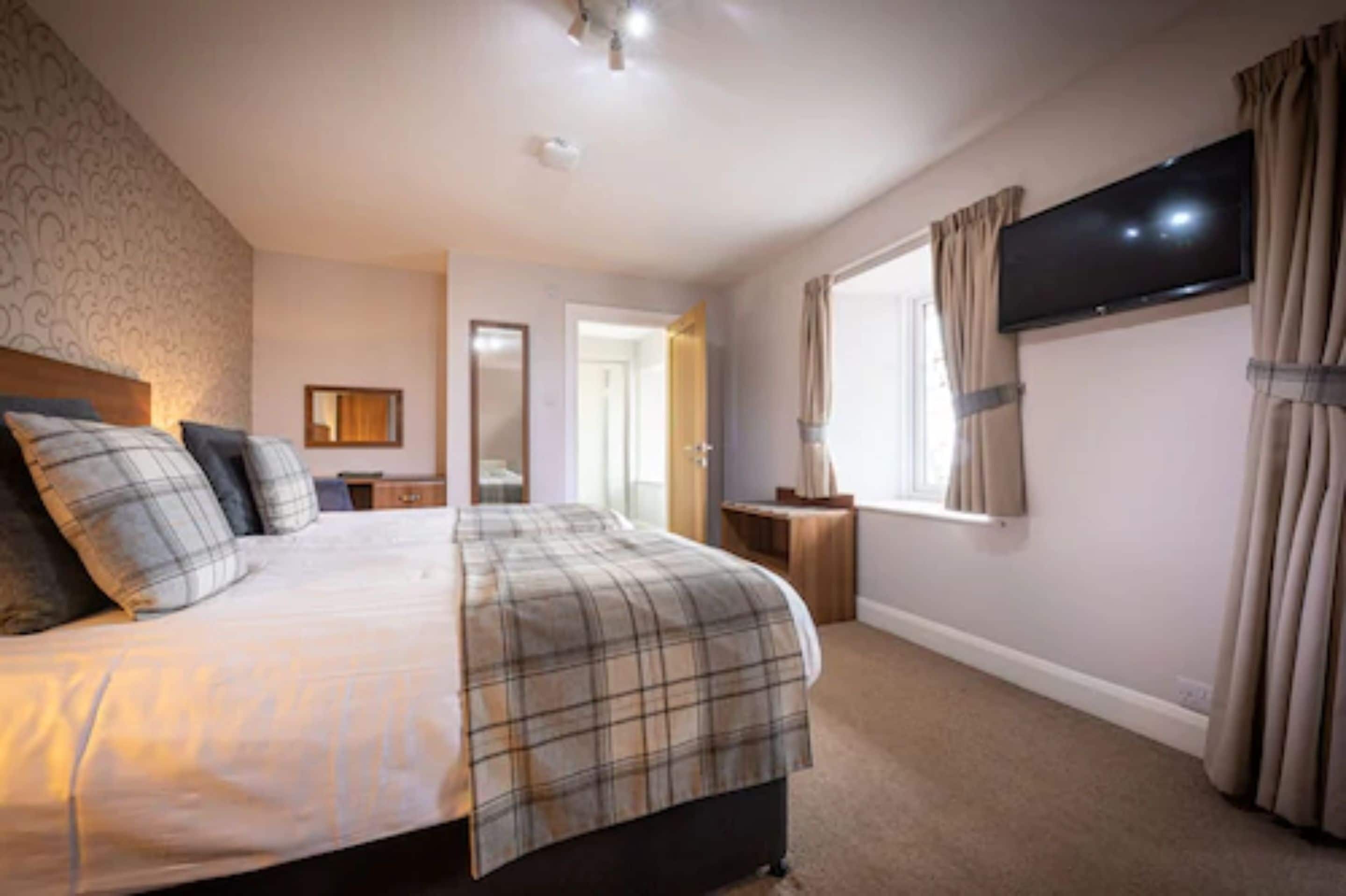A bedroom with a bed, a television mounted on the wall, and a window with curtains.