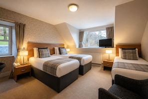 A hotel room with two beds, a television, and a window with curtains.