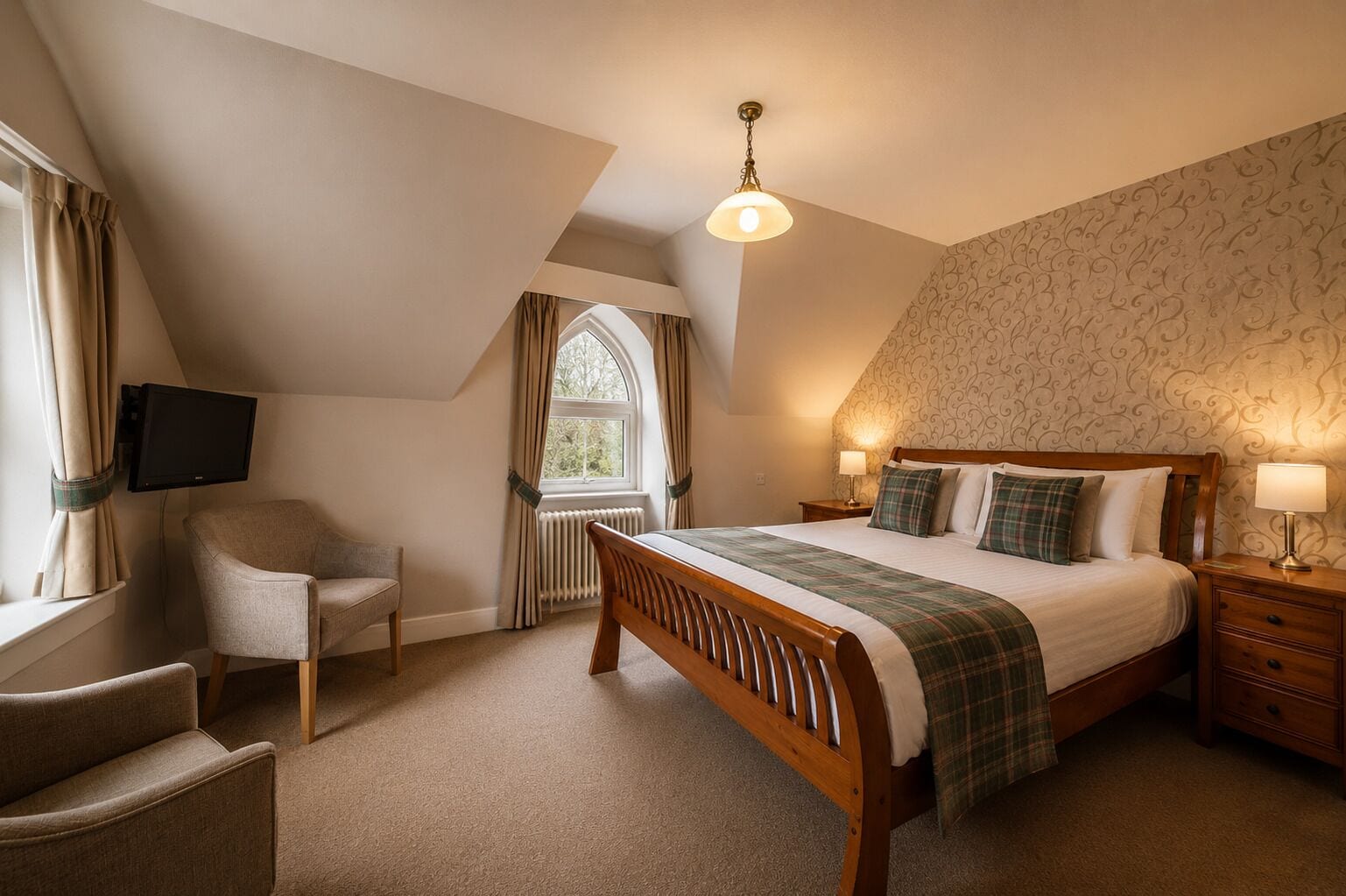 A bedroom with a bed, a chair, a bedside table, a lamp, a television mounted on the wall, and a window with curtains.
