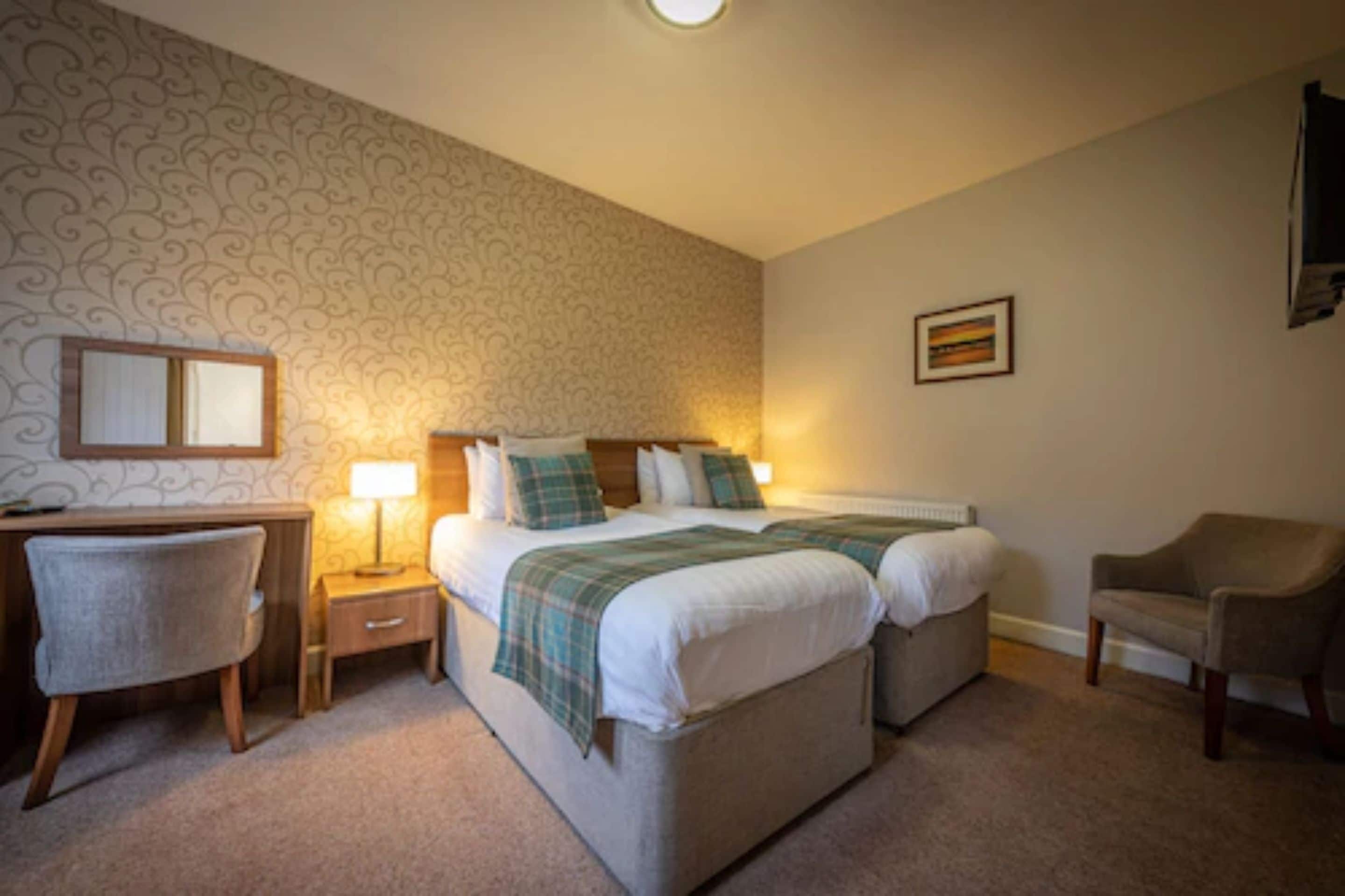 A bedroom with two beds, a desk, a chair, and a lamp.