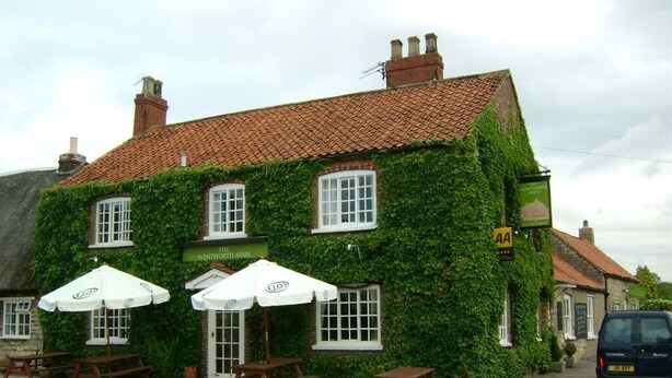 A building with ivy-covered walls and a traditional tiled roof. There are outdoor tables and umbrellas, and a sign indicating 'The Twentworth Arms'. - The Wentworth Arms (Malton)