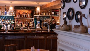 A bar area with a wooden counter, shelves of liquor bottles, a beer tap, and a fireplace with decorative vases. - White Hart Inn (Wells)