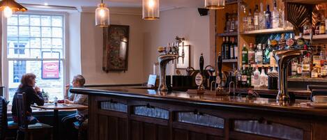 A bar area with a wooden counter, multiple taps, and a variety of bottles.