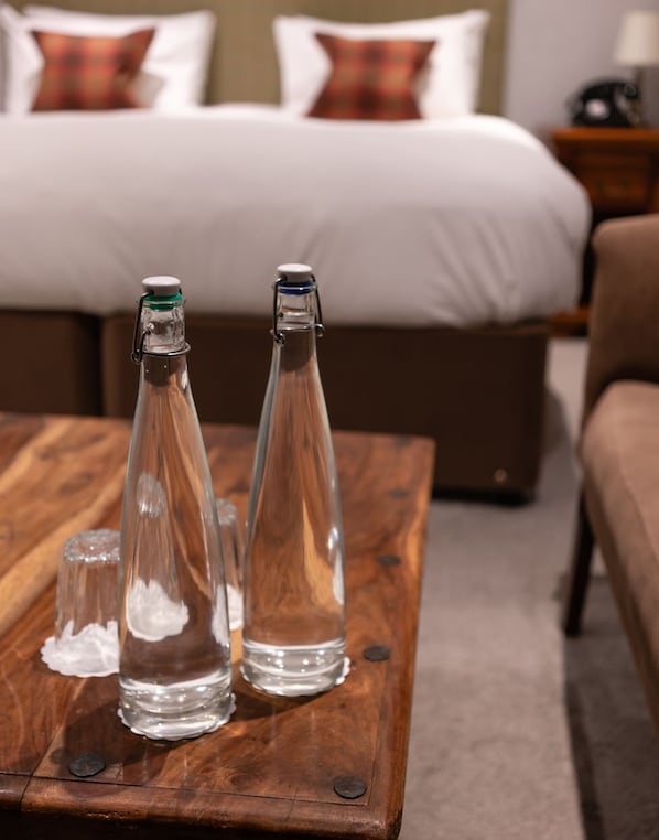 A wooden coffee table with three clear glass bottles and a salt shaker. In the background, there is a bed with white bedding and plaid pillows. - White Hart Inn (Wells)