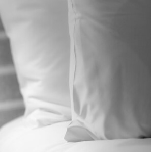A close-up of a white bed with a neatly made pillow.