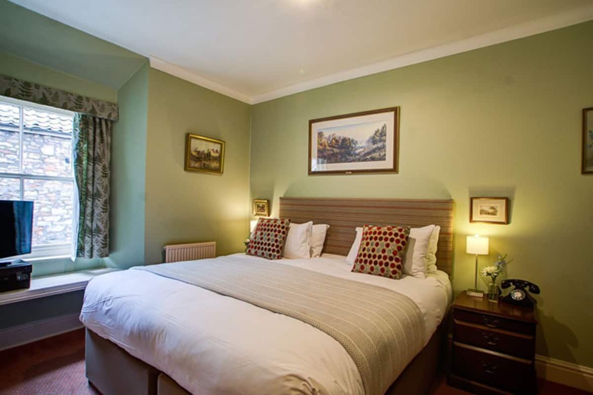 A neatly arranged bedroom with a bed, bedside tables, a window with curtains, and framed pictures on the wall.