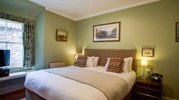 A neatly arranged bedroom with a large bed, a bedside table with a lamp, and a window with curtains.