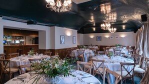 A restaurant with round tables set for dining, wooden chairs, and chandeliers. - White Hart Inn (Wells)