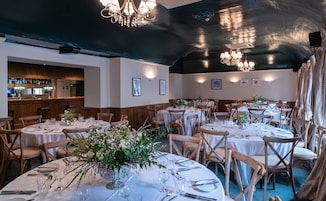 Un restaurante con mesas redondas dispuestas para comer, sillas de madera y candelabros.
