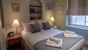 A neatly arranged bedroom with a bed, two bedside tables, a lamp, a telephone, and a window with blinds. - White Hart Inn (Wells)