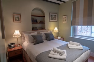 Un dormitorio ordenado con cama, dos mesitas de noche, una lámpara, un teléfono y una ventana con persianas.