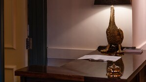A reception desk with a wooden sign above it, a framed abstract painting on the wall, a lamp, and a decorative object on the desk. - White Hart Inn (Wells)