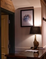 Un mostrador de recepción con un cartel de madera encima, un cuadro abstracto enmarcado en la pared, una lámpara y un objeto decorativo sobre el mostrador.