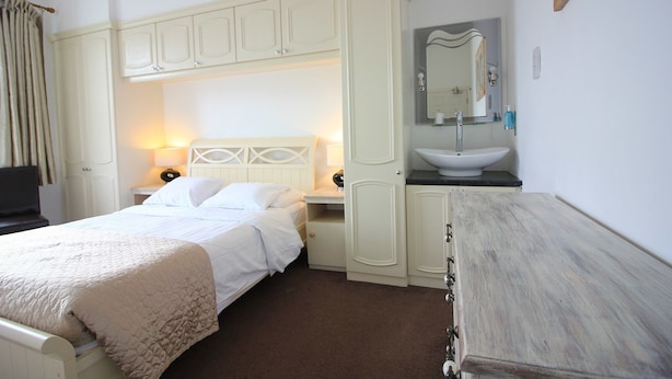 A hotel room with a bed, a bedside table, a dresser, a mirror, and a bathroom with a sink and mirror. - Seafield House (Hove)