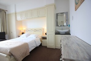 Ein Hotelzimmer mit Bett, Nachttisch, Kommode, Spiegel und einem Badezimmer mit Waschbecken und Spiegel.