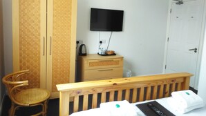 A bedroom with a wooden wardrobe, a television mounted on the wall, a bedside table with a kettle, and a bed with towels. - Seafield House (Hove)