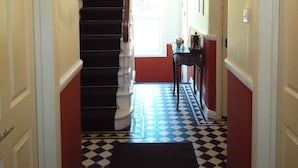 A hallway with a black and white checkered floor, a staircase with red walls, and a chandelier. - Seafield House (Hove)