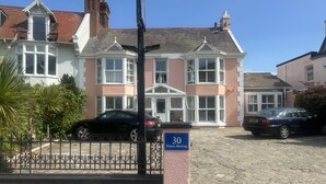 A two-story building with a pink facade, a black car parked in front, and a sign indicating the address "30 Potters Mooring". - Potters Mooring Guest House Hotel (Teignmouth)