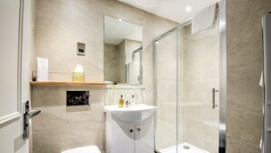 A modern bathroom with a toilet, a glass shower enclosure, and a vanity with a mirror. - Potters Mooring Guest House Hotel (Teignmouth)