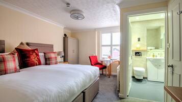 Habitación de hotel con una cama grande, una silla roja, una mesita y un baño visible a través de una puerta abierta.