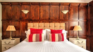 A bedroom with a large bed, wooden paneling on the walls, two bedside tables with lamps, and a red and beige striped throw blanket. - Potters Mooring Guest House Hotel (Teignmouth)