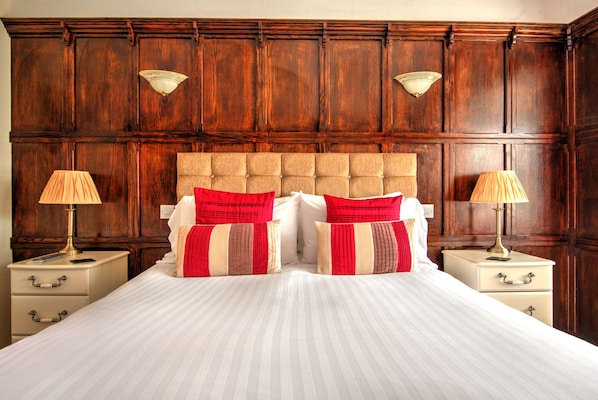 Un dormitorio con una cama grande, paneles de madera en las paredes, dos mesitas de noche con lámparas y una colcha a rayas beige y roja.