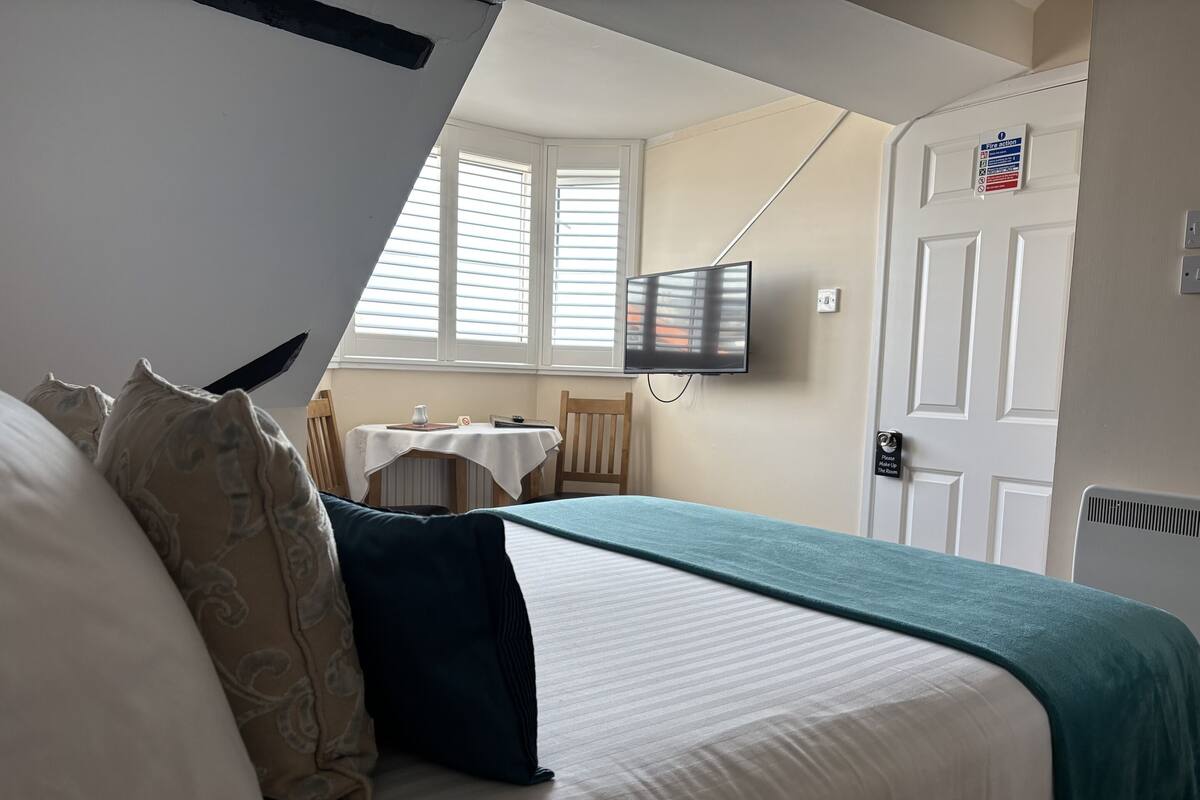 Une chambre à coucher comprenant un lit, une télévision, une petite table et une fenêtre avec des stores.