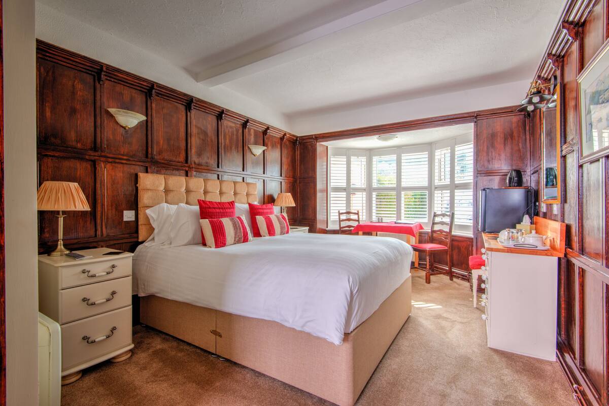 Une chambre à coucher avec un grand lit, des lambris en bois, un bureau avec une télévision et une fenêtre équipée de stores.