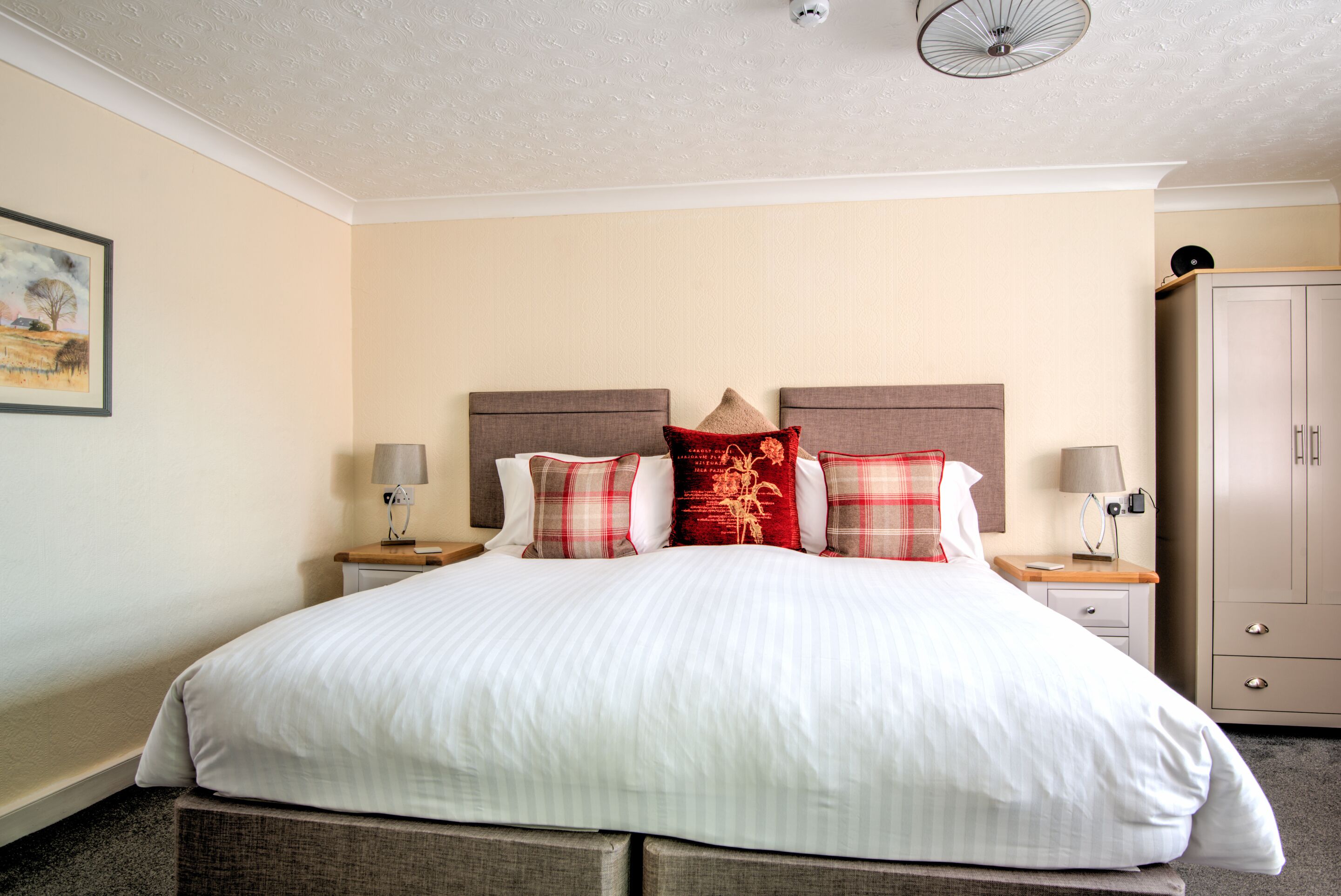 A neatly made bed with a white duvet, two nightstands with lamps, and a wardrobe in a hotel room.