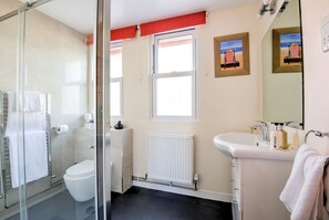 Une salle de bain moderne avec une douche à l’italienne en verre, des toilettes, un lavabo avec des articles de toilette et une fenêtre donnant sur la plage.