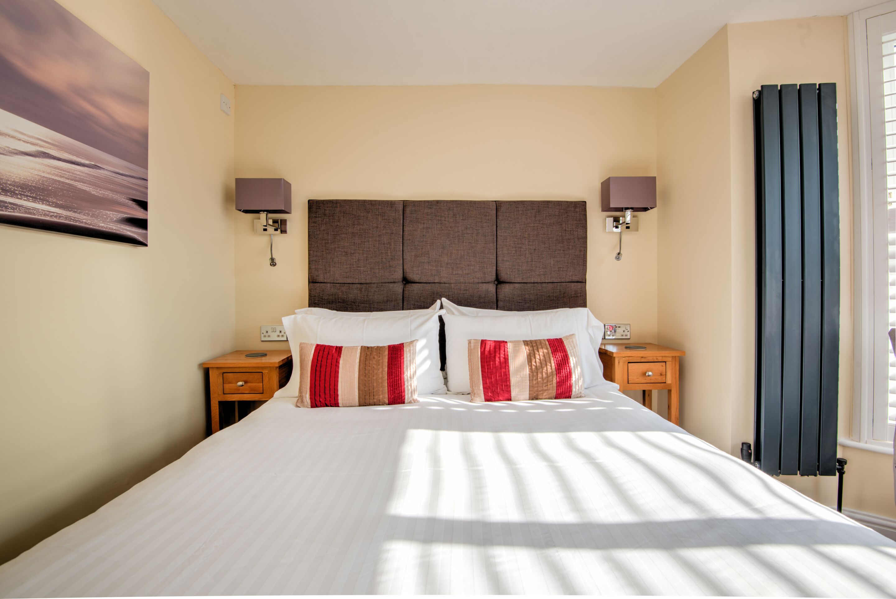 A hotel room with a large bed, two bedside tables, a headboard, wall-mounted lamps, and a window with curtains.