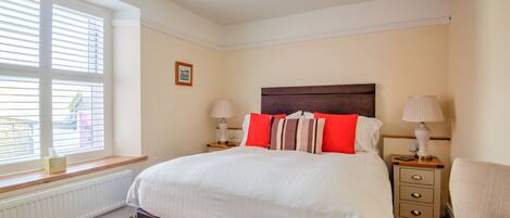 A bedroom with a large bed, two bedside tables, a chair, a window with blinds, and a radiator.