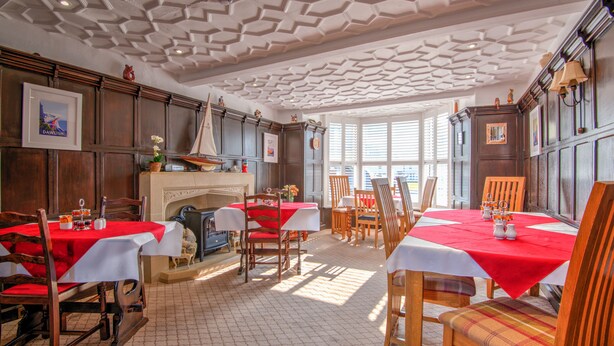 A dining area with wooden furniture, red tablecloths, and a fireplace. - Potters Mooring Guest House Hotel (Teignmouth)