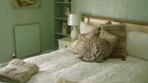 A bedroom with a bed, pillows, a nightstand, a lamp, and a radiator. - The Pack Horse (South Brent)